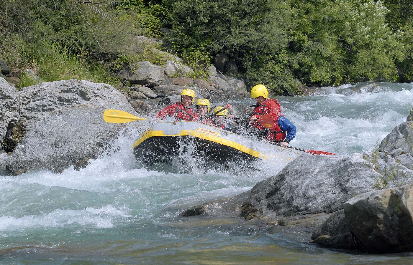 Mehrere mit Helm geschützte Personen beim Rafting im Meraner Land