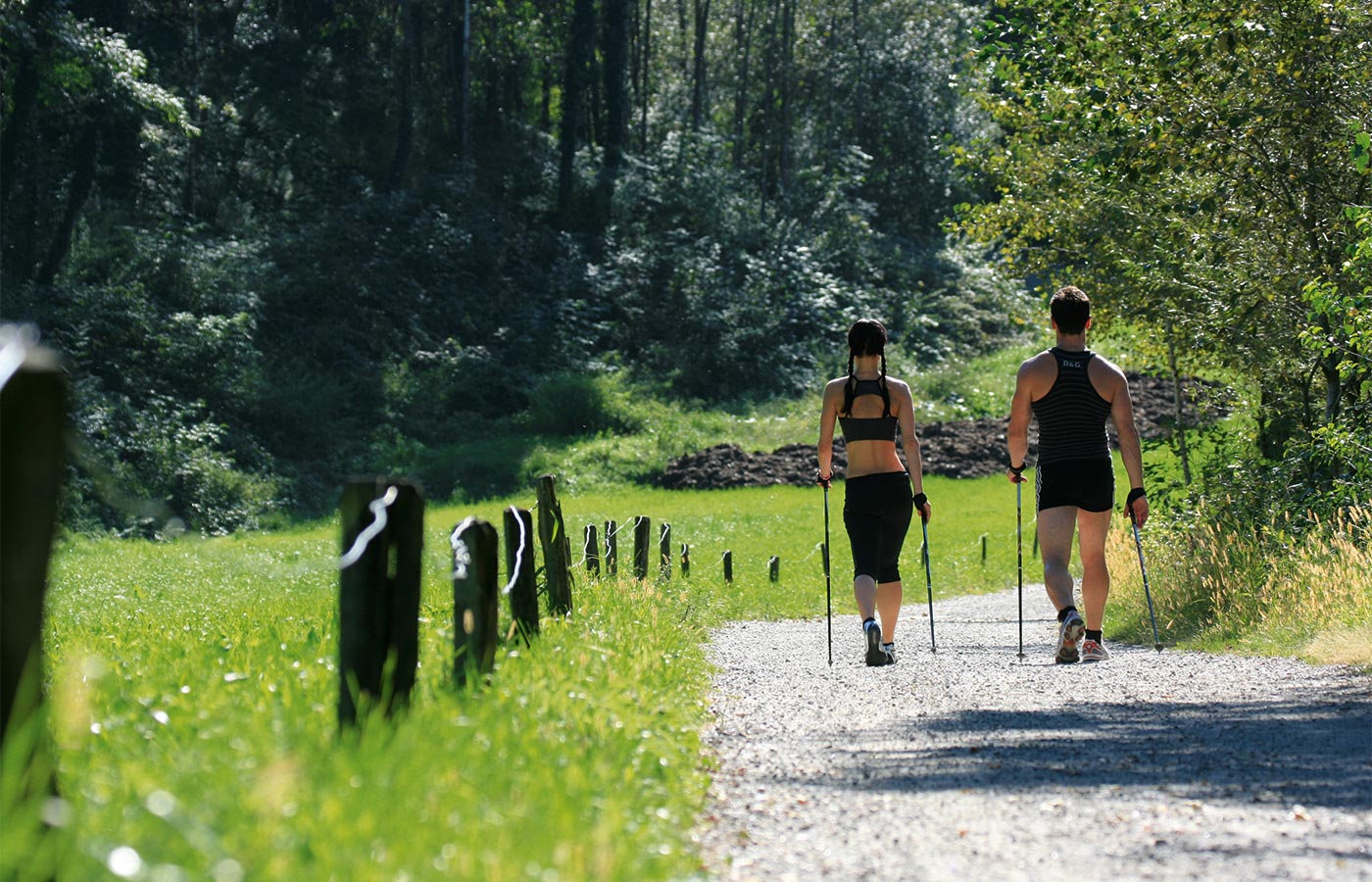 Zwei leicht bekleidete Nordic Walker wandern einen Schotterweg entlang